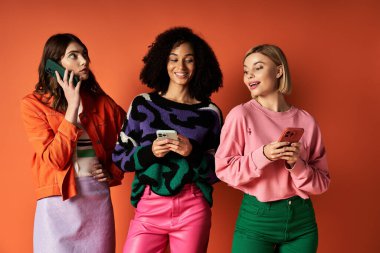 Canlı giyinmiş üç genç kadın, turuncu bir zemin üzerinde birleşmiş, dostluk ve kültürel çeşitliliği somutlaştırıyorlar..