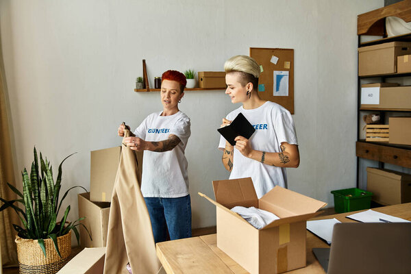 Молодая пара лесбиянок в волонтерских футболках, работающих вместе в помещении для благотворительности.