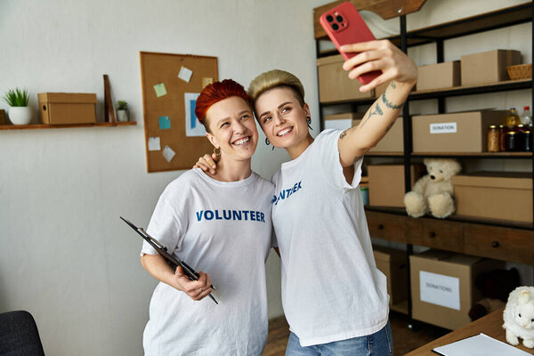 Две женщины, часть молодой лесбийской пары, делают селфи в комнате, когда они вместе добровольно идут в благотворительных футболках.