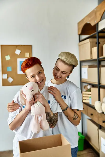 stock image A woman holding a stuffed animal affectionately stands next to a partner, both engaged in a heartwarming moment.