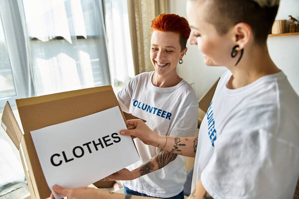 Two women in volunteer t-shirts standing together with pride and unity as they work on a charity project.