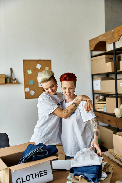 A young lesbian couple in volunteer t-shirts are standing together in a room, engaged in charity work.
