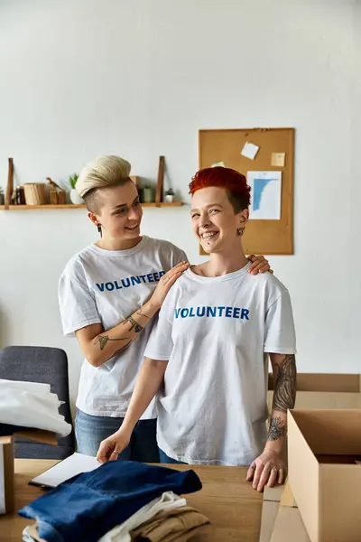 stock image Two women in volunteer t-shirts standing united in a room, working together for a cause they believe in.