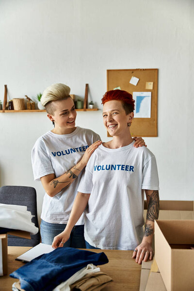 Две женщины в футболках-волонтерах стоят в одной комнате и работают вместе ради дела, в которое верят..