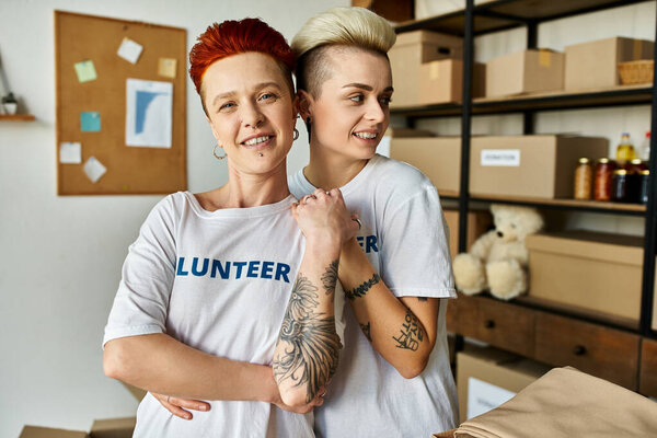 Молодая пара лесбиянок, одетая в футболки-волонтеры, стоят вместе во время благотворительной деятельности.