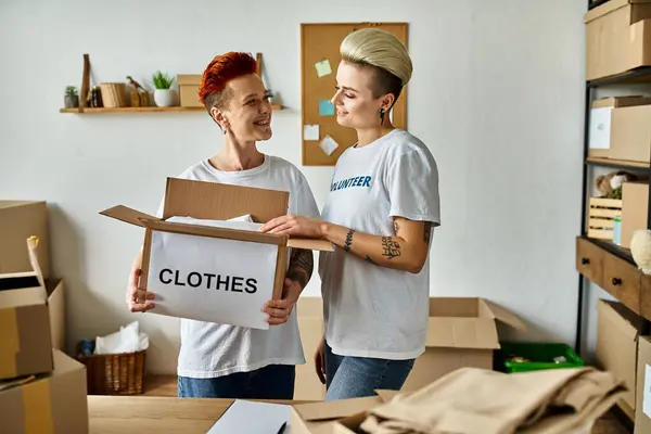 stock image Young lesbian couple in volunteer t-shirts standing together, engaged in charity work in a room.