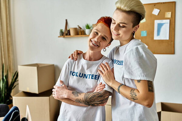 Две молодые женщины, часть пары ЛГБТК, стоят бок о бок в футболках добровольцев, работая вместе на благотворительность.