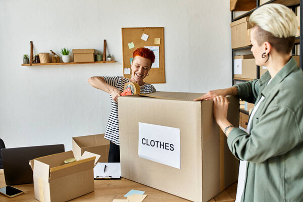 women standing next to a cardboard box with clothes on it, engaged in charity work.