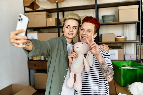 stock image Two women take a selfie with a stuffed animal, sharing a moment of joy and connection amidst their charity work.