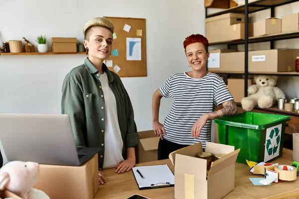 stock image Two young women, a lesbian couple, standing together in a room, working on a charity project.