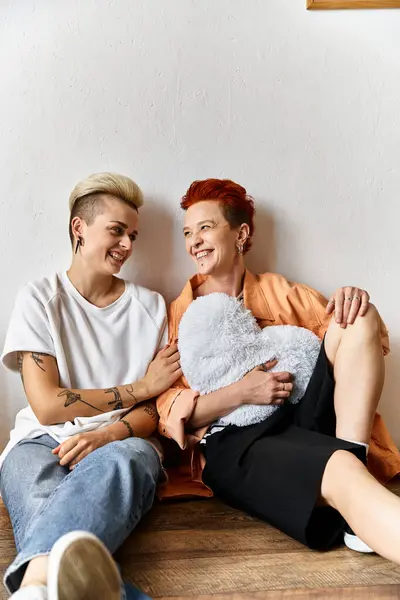 stock image A young lesbian couple sitting side by side in a volunteer center surrounded by boxes, engaging in charity work.