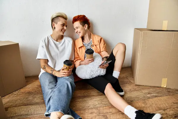 Stock image A young lesbian couple sitting on the floor together in a volunteer center surrounded by charity donation boxes.