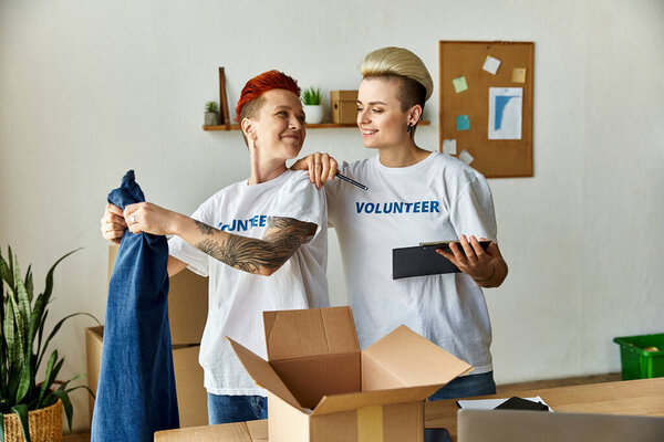 Молодая пара лесбиянок в футболках-волонтерах, работающих вместе на благотворительность в комнате.