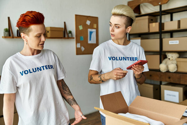 Молодая пара лесбиянок, обе в волонтерских футболках, стоят бок о бок, объединившись в своих усилиях по благотворительности.