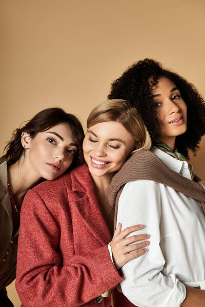 Молодые, красивые женщины разных культур позируют вместе в стильной одежде на бежевом фоне.