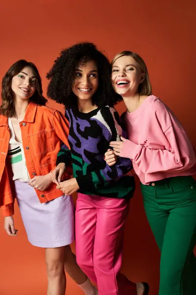 stock image Three young, beautiful women in vibrant clothes of diverse cultures pose together on an orange background.