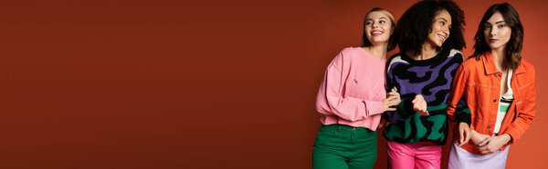 Молодые, мультикультурные женщины в яркой одежде стоят вместе на оранжевом фоне.