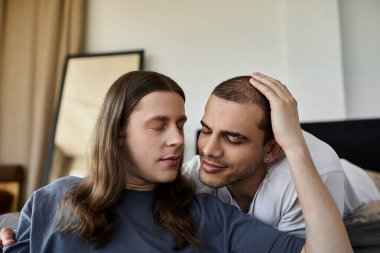 A young gay couple shares a tender moment in their bedroom, displaying love and affection. clipart