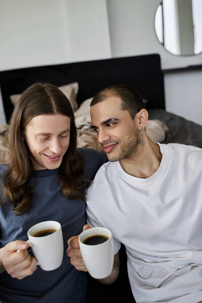 Молодая гей-пара наслаждается уютным утром вместе, потягивая кофе и делясь любовью в своей спальне.