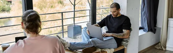 stock image A young gay couple spends a relaxed afternoon together in their modern home, working on laptops by a large window.