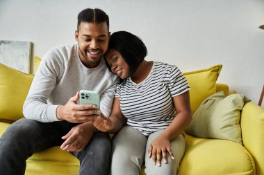 Afro-Amerikalı bir çift koltuklarında oturup birlikte telefona bakmaktan zevk alıyor..
