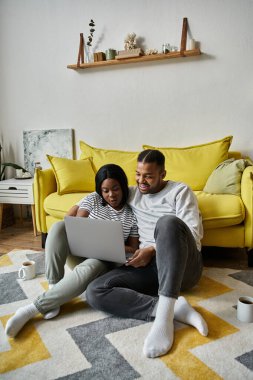 Sevgi dolu bir çift, sarı bir kanepenin önünde dizüstü bilgisayarda geziniyor..