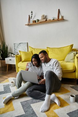 Afro-Amerikalı bir çift sarı bir kanepenin önünde birlikte dizüstü bilgisayar kullanıyor..