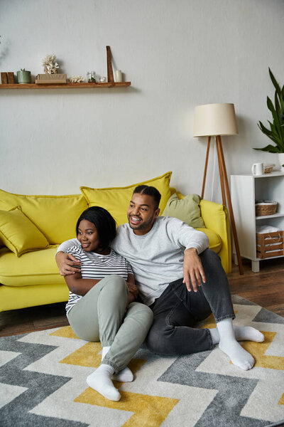 A loving couple sits on a rug in their home, enjoying each others company.