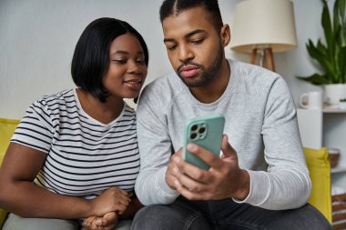 Sevgi dolu bir Afro-Amerikan çifti, akıllı telefonlarına dalmış bir kanepede oturuyor..