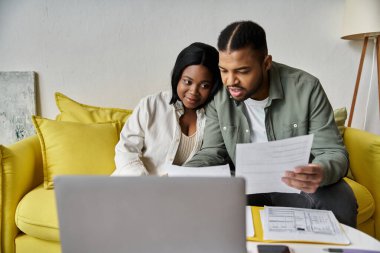 Sevgi dolu bir Afrikalı Amerikalı çift kanepede oturup evrakları gözden geçirir ve bir dizüstü bilgisayar kullanır..