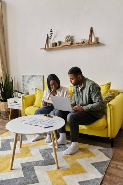 Bir çift sarı koltukta rahatlar, dizüstü bilgisayarı paylaşırlar ve birlikte eğlenirler..