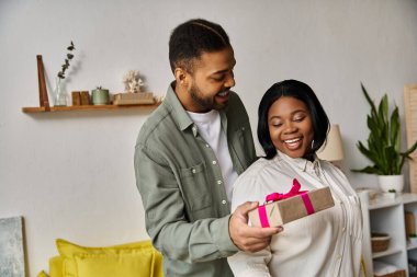 A man gives a gift to a woman in their home. clipart