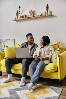 Sevgi dolu bir Afrikalı Amerikalı çift evlerindeki sarı bir kanepede dinlenirken gülümsüyor ve sohbet ediyor..