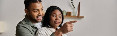 Mutlu Afrika kökenli Amerikalı çift gülüyor ve ekranın dışında bir şeye işaret ediyor..