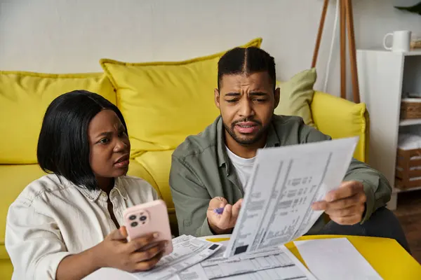 stock image A couple sits together on a couch at home, reviewing paperwork.