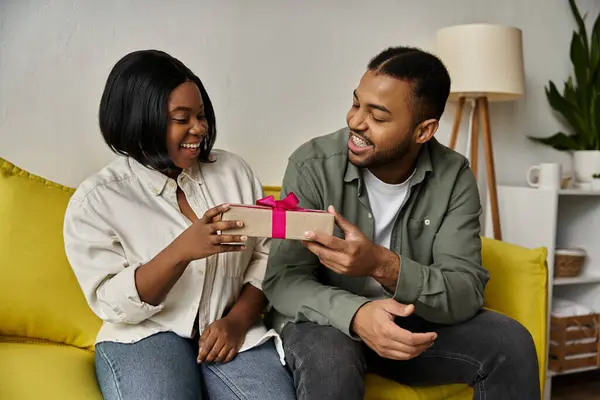 stock image A happy couple smiles at each other while exchanging a gift.