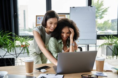 Two women working together on a laptop in an office. clipart