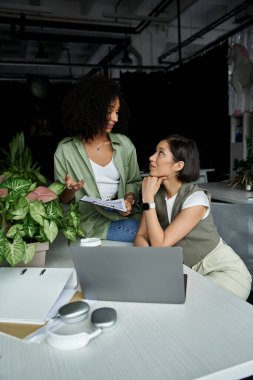 Two women working together on a project in an office setting. clipart