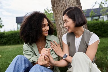 Two women, sitting by a tree, share a moment of intimate conversation. clipart