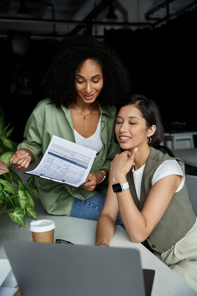 Two women in office attire collaborate at a desk.