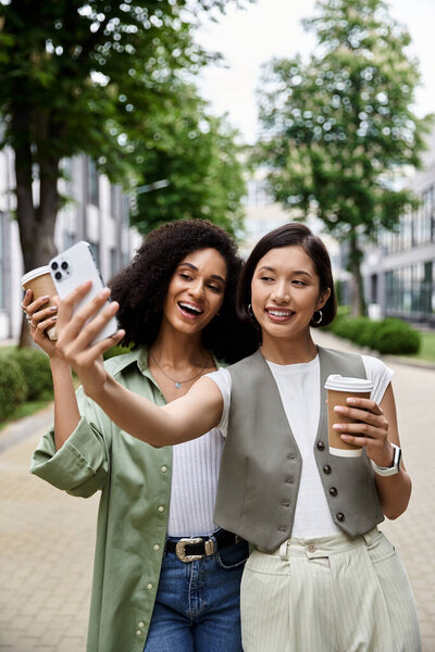 Две женщины делают селфи, держа кофейные чашки..