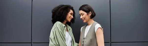 stock image Two women in business casual smile in front of a grey wall.