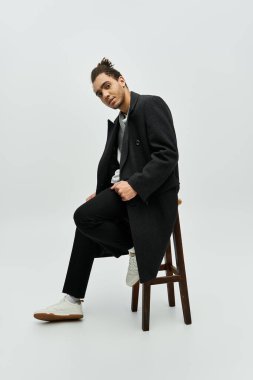 Afrikalı Amerikalı bir erkek model gri bir arka plana karşı şık bir siyah ceket giyiyor..