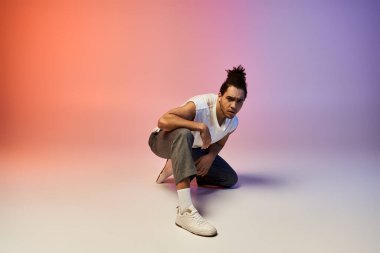 Genç bir Afrikalı Amerikalı erkek dansçı canlı pembe ve mor bir arka plana karşı dinamik bir konumda poz verir..