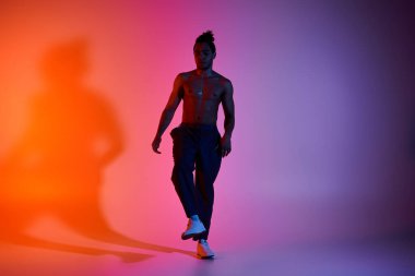 Genç bir Afro-Amerikalı adam pembe ve turuncu bir arka planda dans ediyor. Siyah pantolon ve beyaz ayakkabı giyiyor..