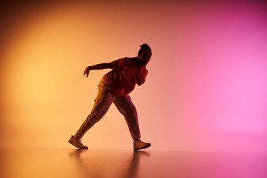 Afro-Amerikalı bir erkek dansçı, turuncu ve pembe renkli bir arka plana karşı bir hareket sergiliyor..