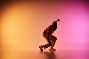 Afrikalı Amerikalı bir erkek dansçı canlı bir turuncu ve pembe ışıklandırmaya karşı dinamik bir hareket sergiliyor..