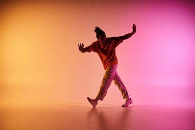 Sıradan kıyafetli genç bir Afrikalı Amerikalı, parlak sarı, turuncu ve pembe arka planda dans ediyor..