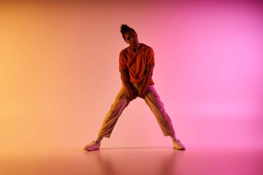 Genç bir Afrikalı Amerikalı erkek dansçı, sarı, turuncu ve pembe arka planda poz verir..
