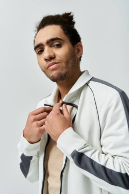 Gri arka planda gri aksanlı beyaz ceketli genç bir Afrikalı Amerikalı poz veriyor..